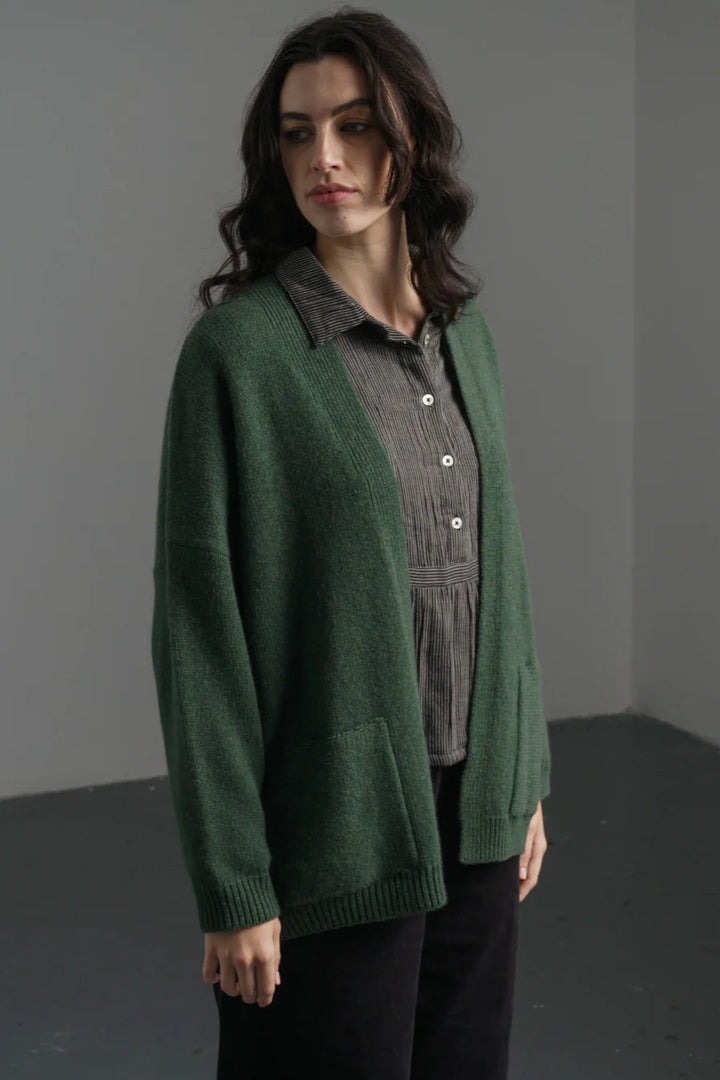 Woman wearing a green cardigan over a gray shirt in a minimalistic setting