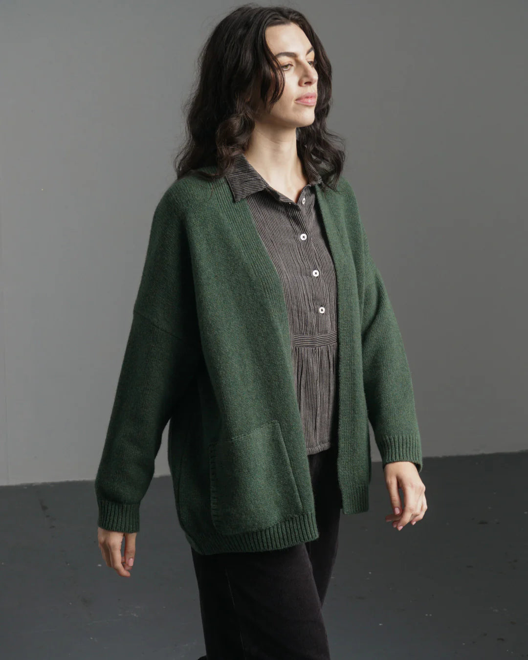 Woman wearing a green cardigan over a plaid shirt against a gray background