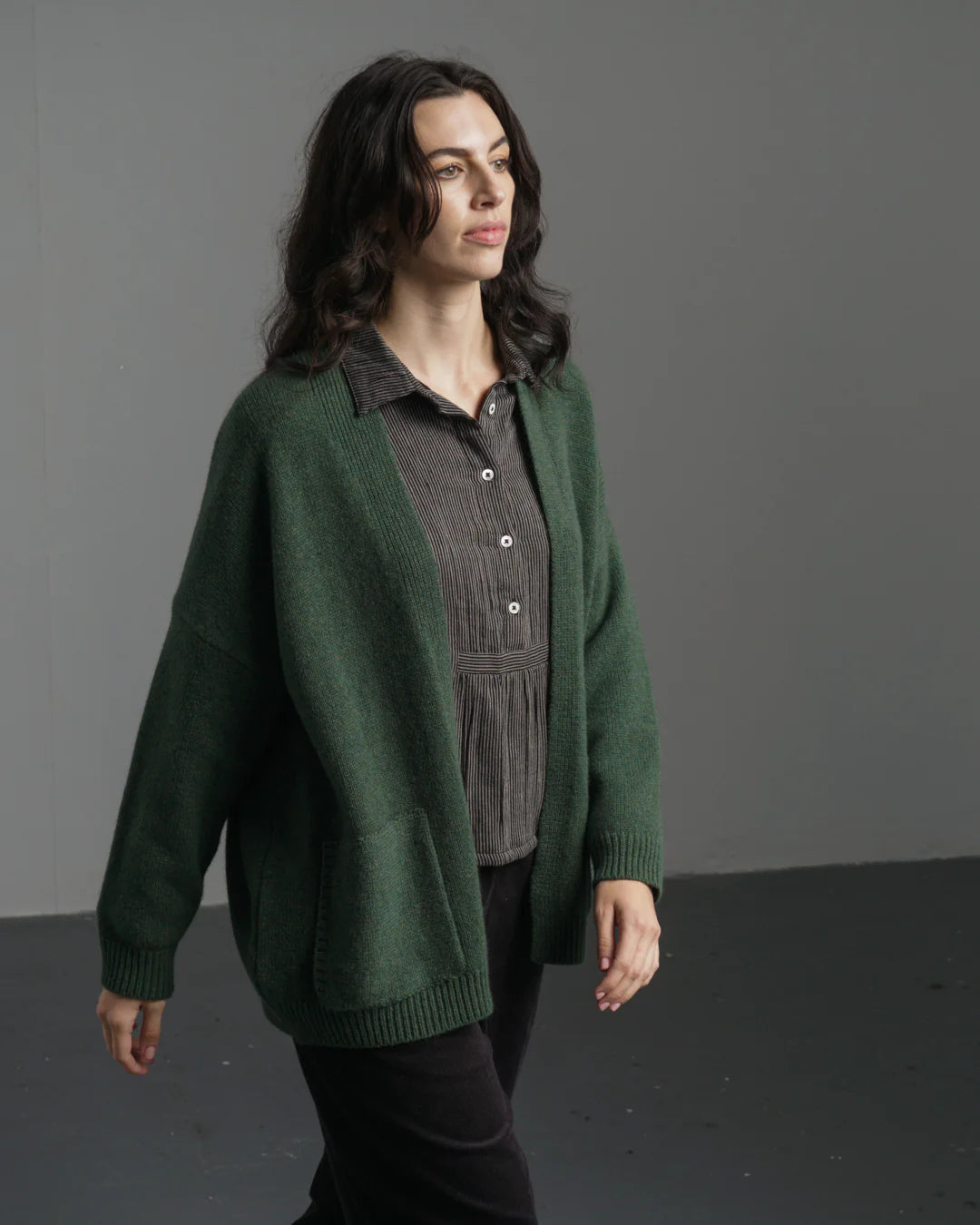 Woman wearing a green cardigan over a gray shirt against a gray background