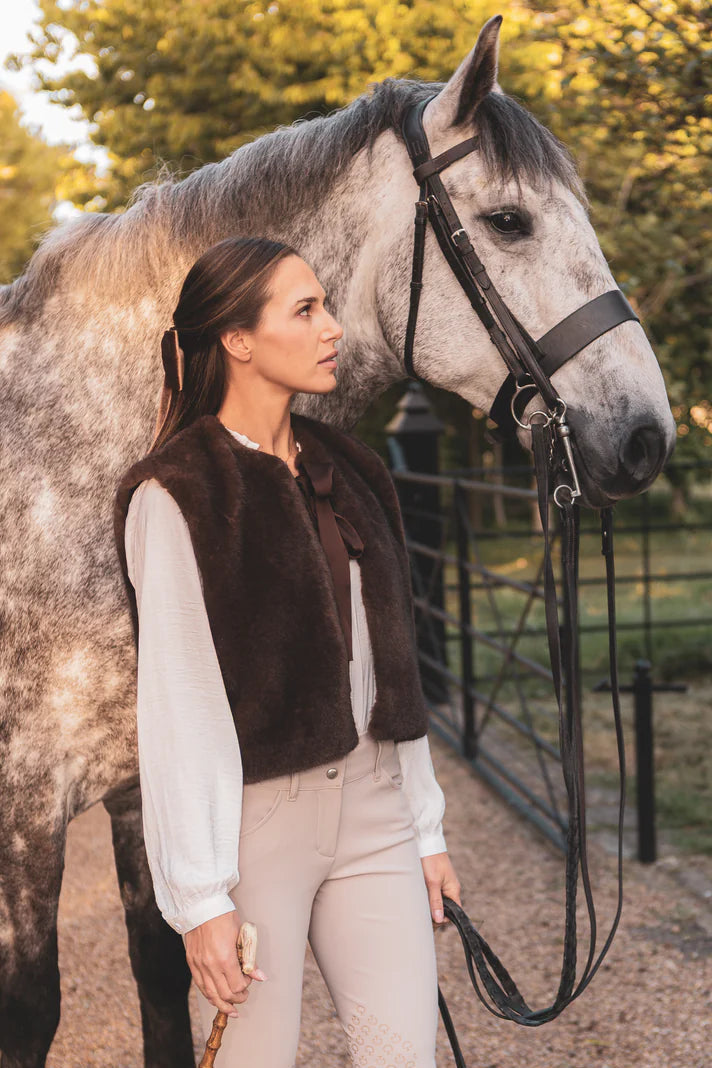 Woman in equestrian attire standing next to a horse in an outdoor setting