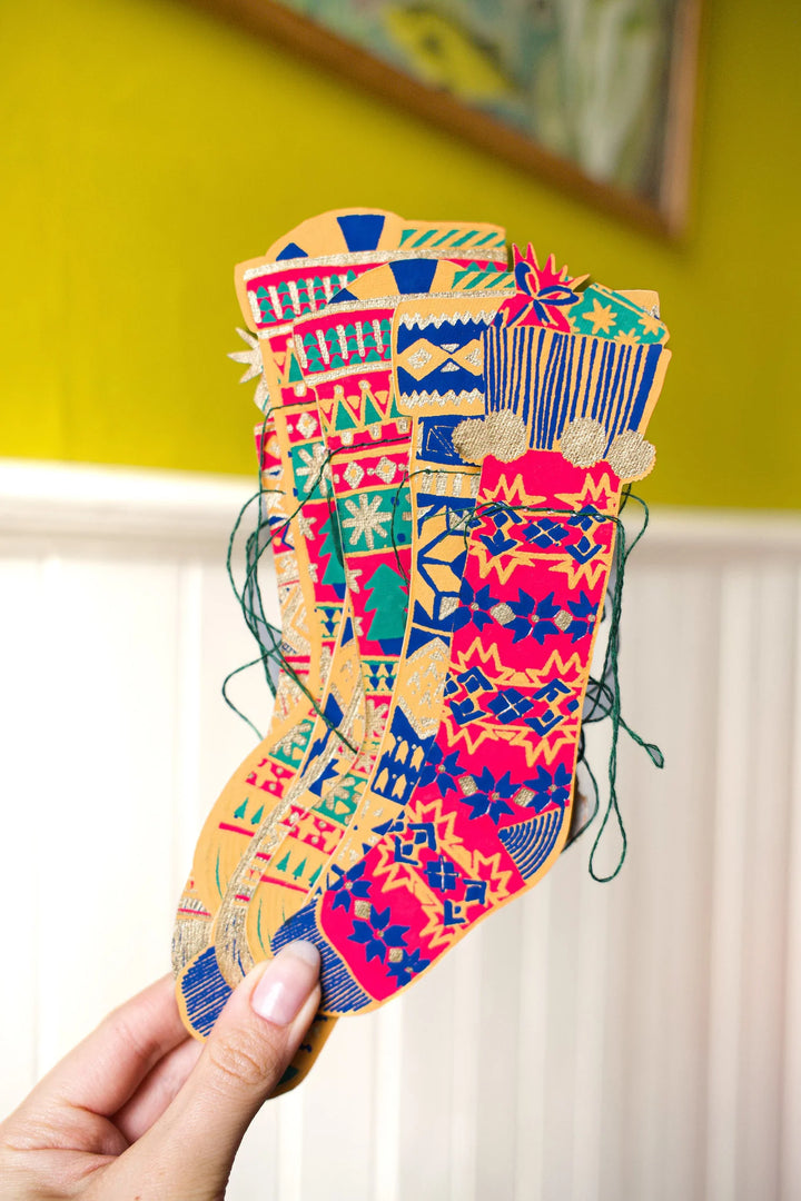 Colorful patterned stockings garland held by a hand against a yellow wall.