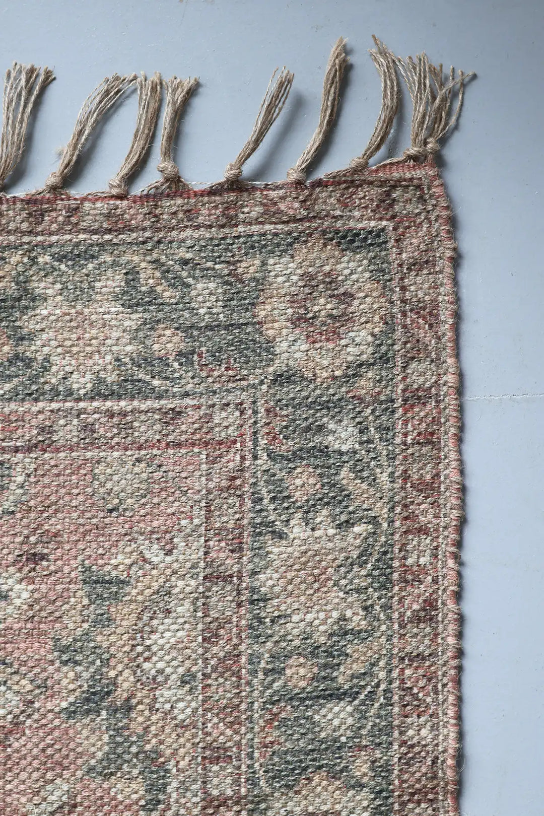 Close-up of a textured rug with tassels on a plain background