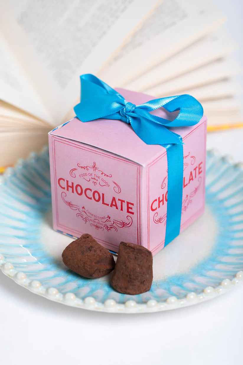 Pink chocolate box with a blue ribbon on a decorative plate with chocolate truffles.