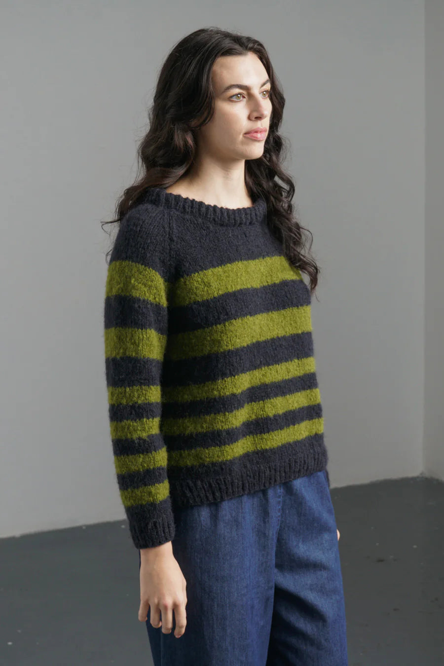 Woman wearing a striped sweater and blue pants against a plain background