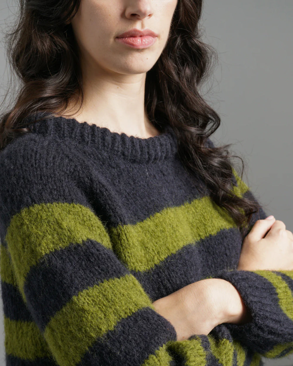 Person wearing a navy and green striped sweater against a grey background