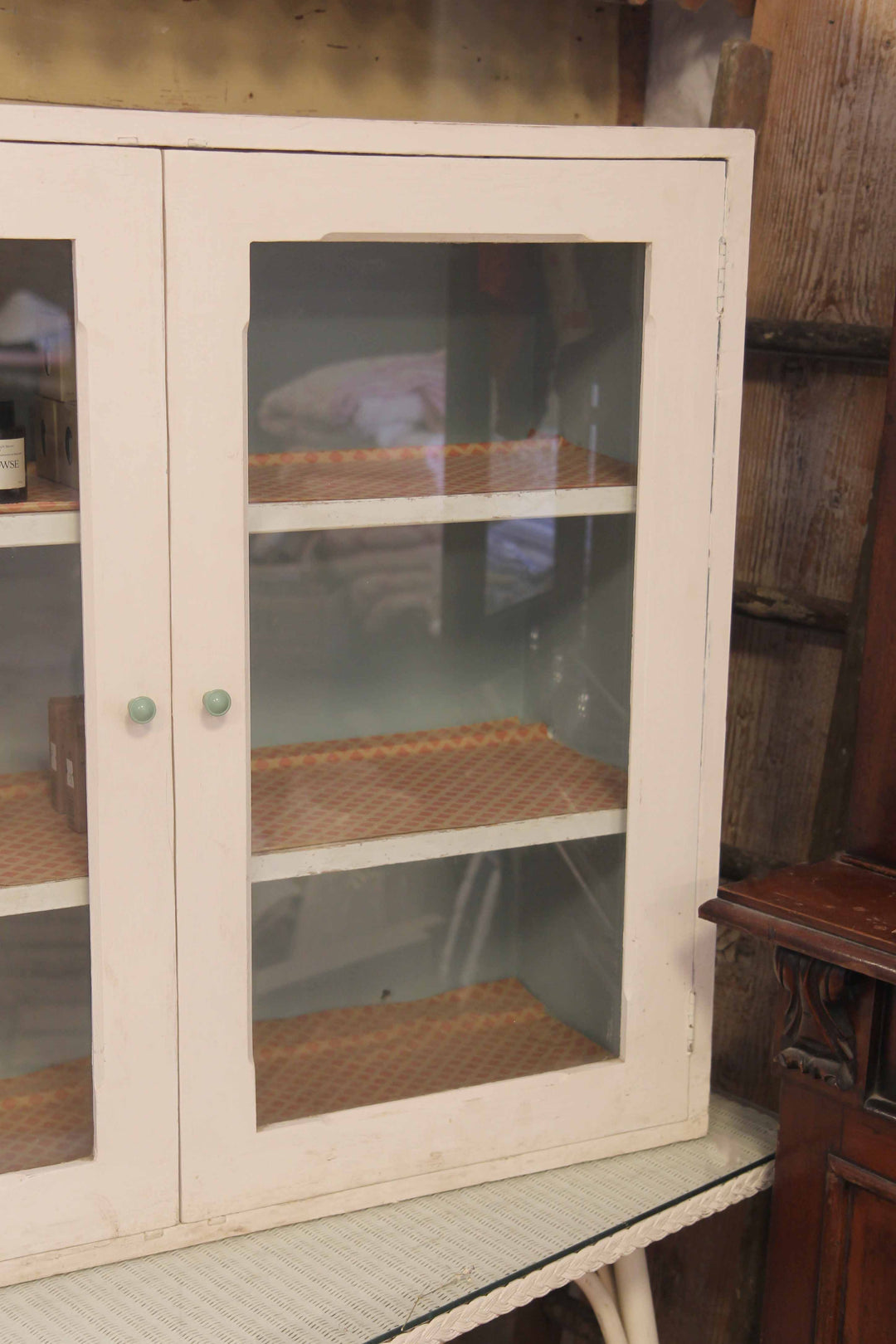 Vintage-style glass-front cabinet with wire mesh shelves on a wooden floor.
