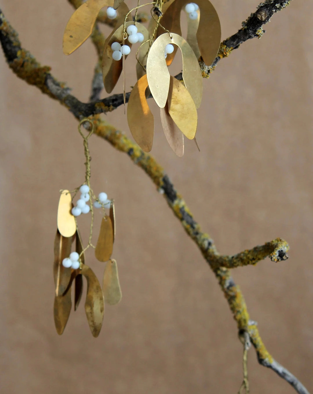 small brass mistletoe tree decoration with white beads hanging on a branch