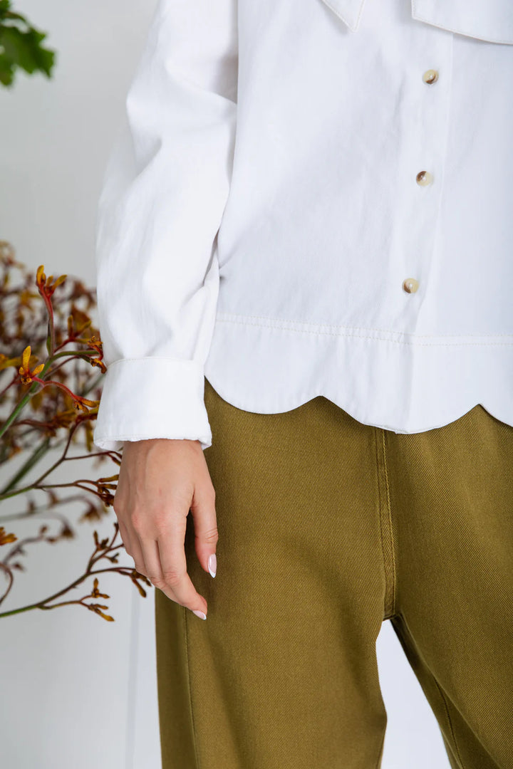 Person wearing a white blouse and green pants with a minimal background