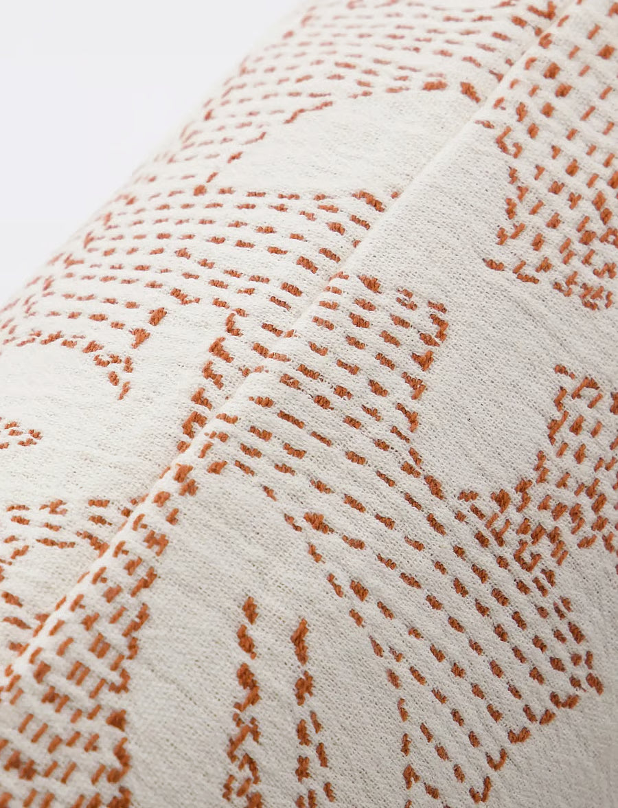 Close-up of a woven textile with a cream base and rust-brown stitched geometric pattern.