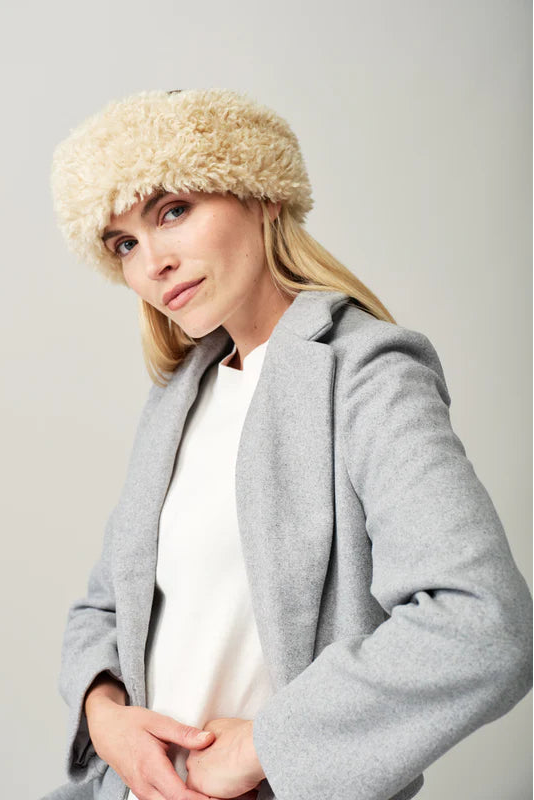 Woman wearing a gray coat and beige fur hat against a plain background