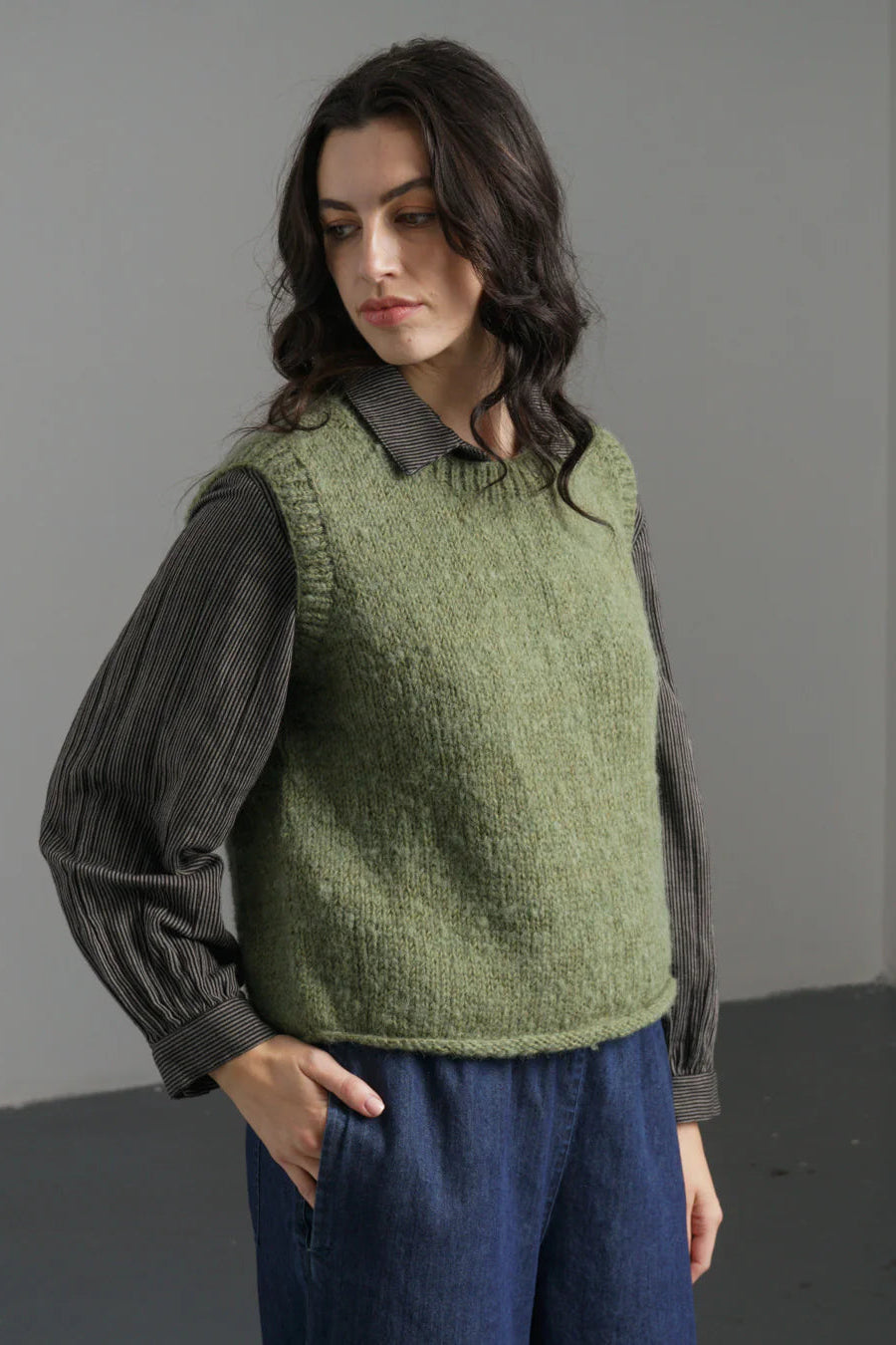 Woman wearing a green knitted vest over a dark shirt with a gray background