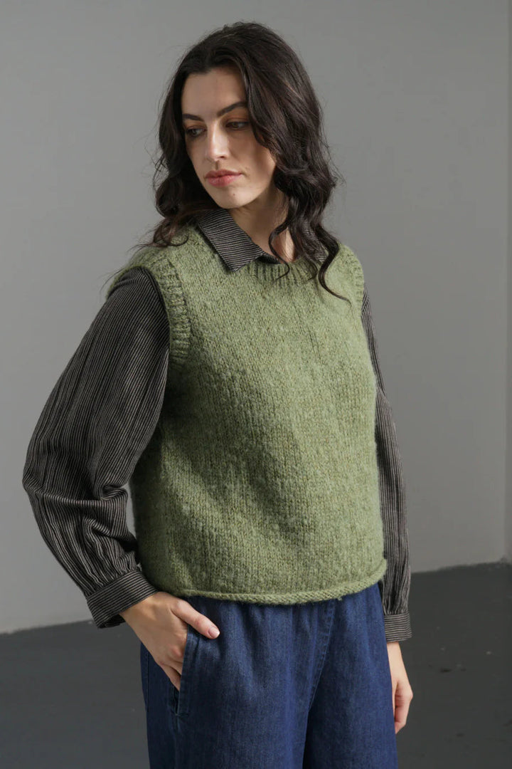 Woman wearing a green knitted vest over a dark shirt with a gray background