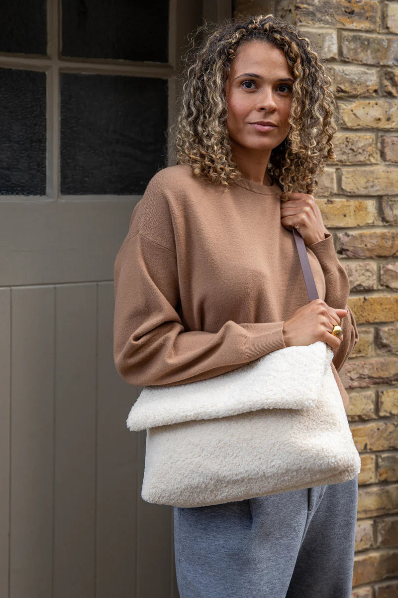 Woman holding a cream-colored bag against a brick wall.