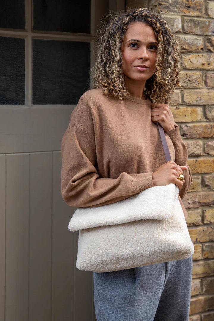 Woman holding a cream-colored bag against a brick wall.