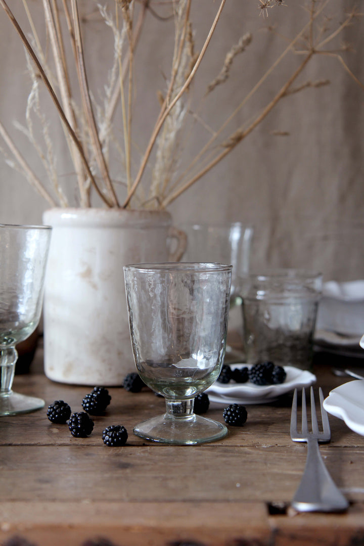Dining table setting with glassware, blackberries, and a vase on a wooden surface.