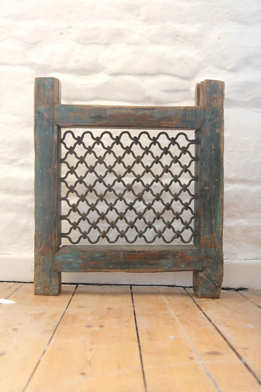 Decorative metal screen with lattice design on a wooden floor against a white wall.