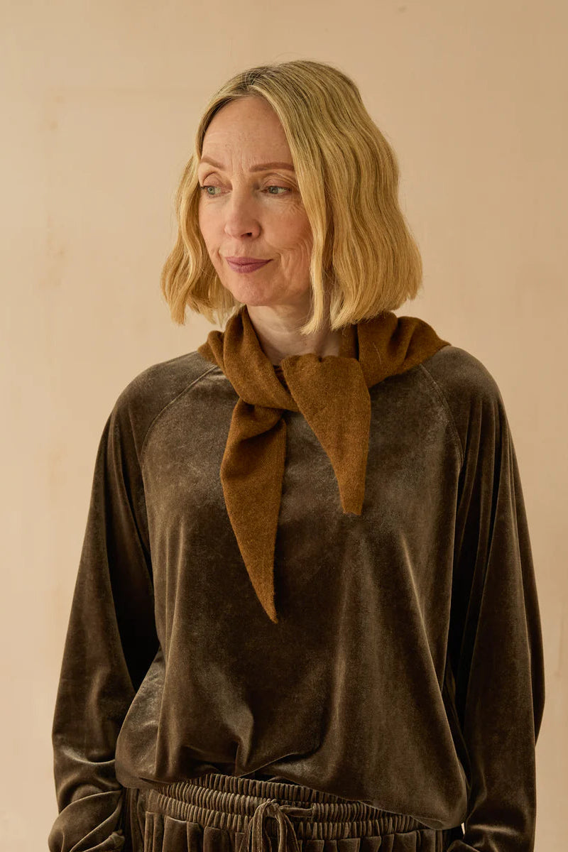 Woman wearing a brown velvet outfit with a matching scarf against a beige background