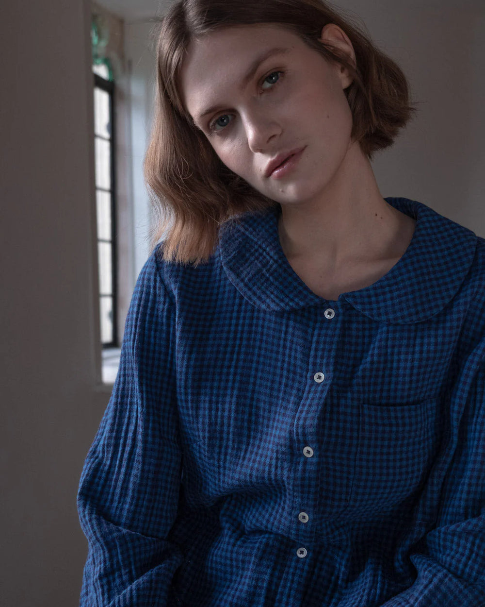 Woman wearing a blue checkered shirt in a softly lit room.