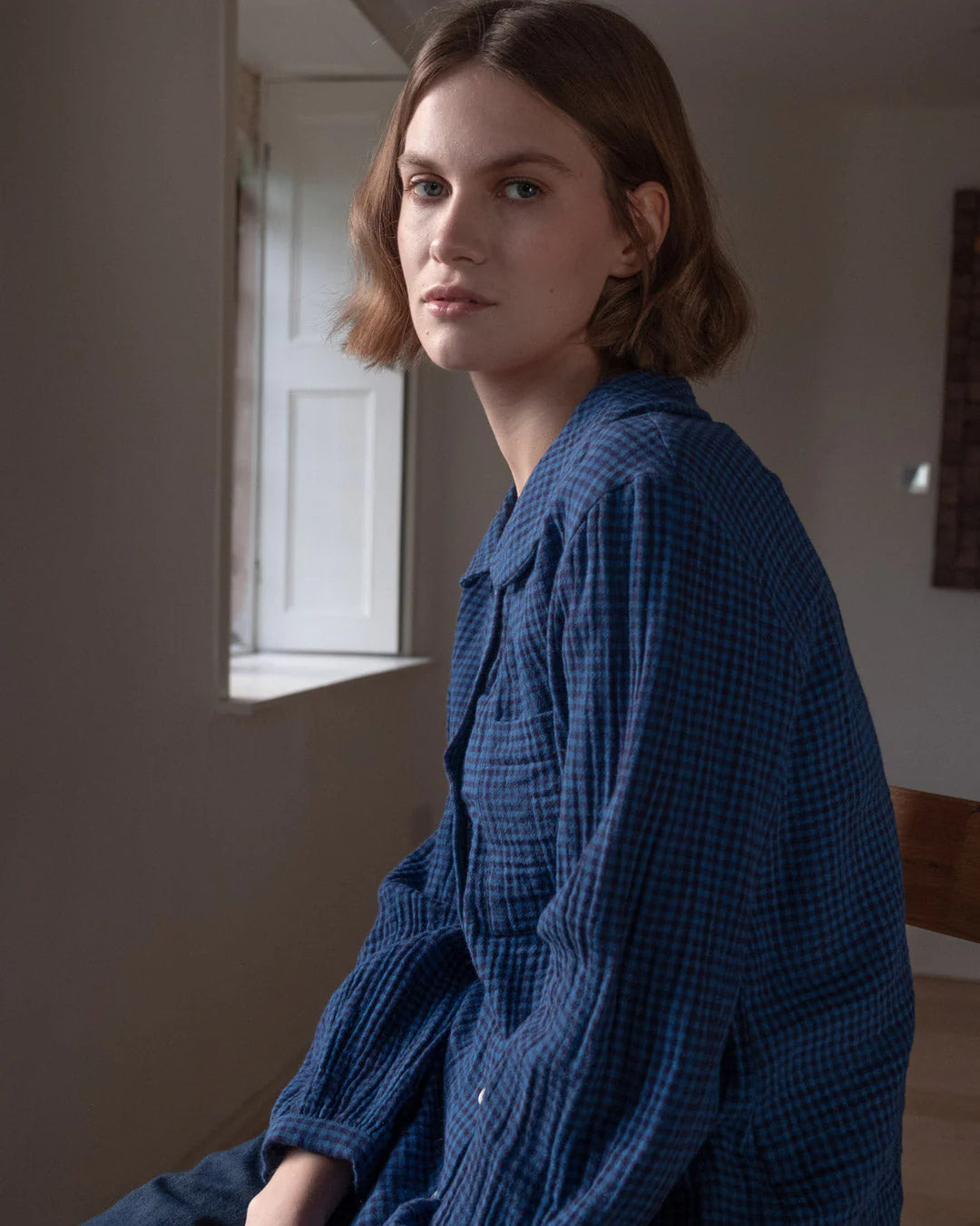 Woman wearing a blue checkered dress sitting indoors.