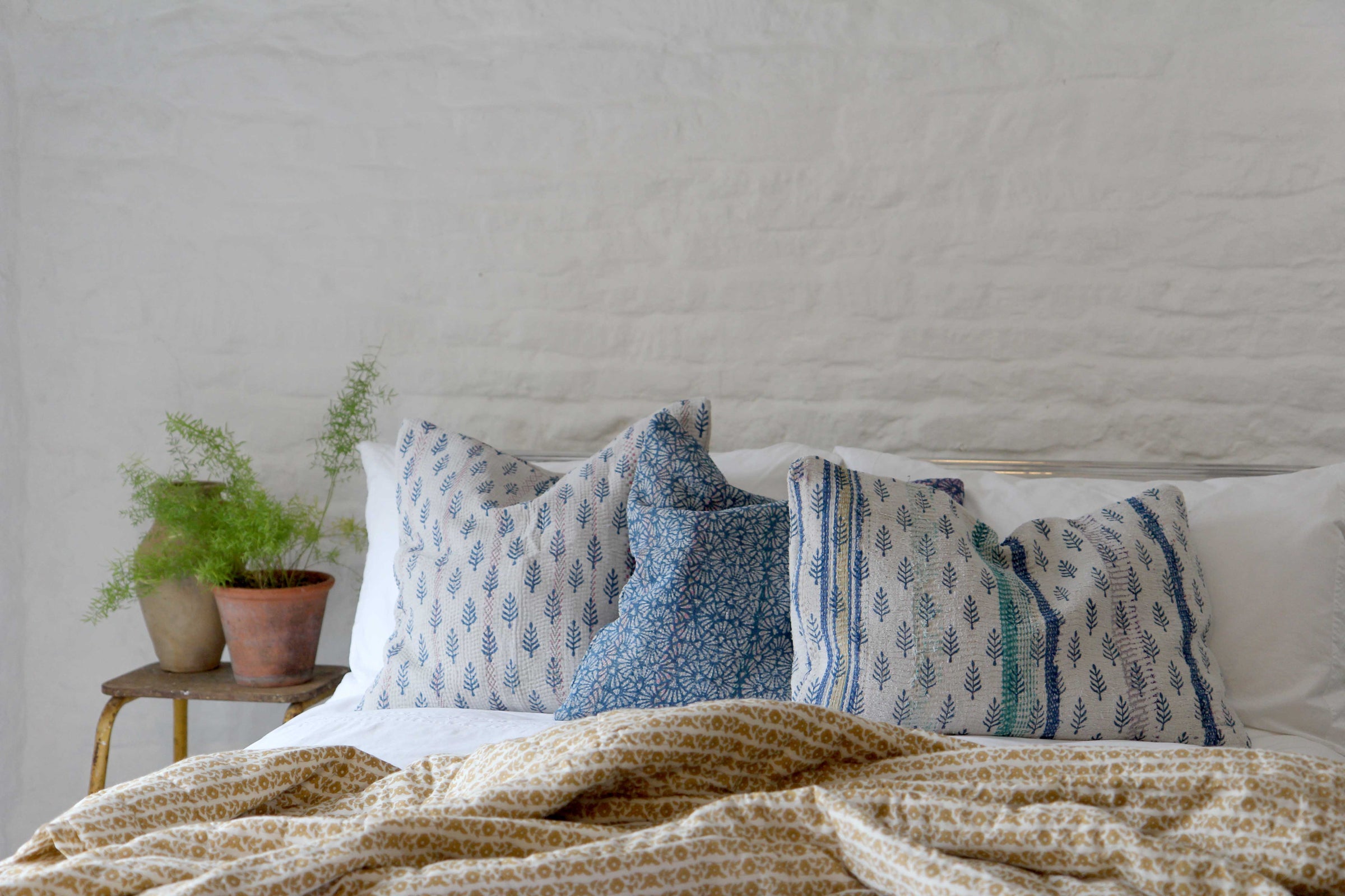 lifestyle group of vintage sari kantha cushions displayed on white bed with throw and pot plant
