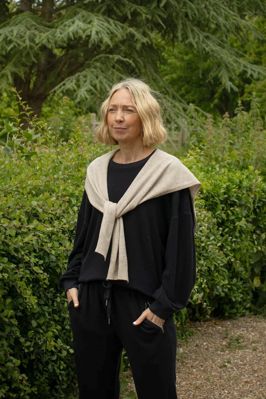 Woman wearing a beige scarf and navy blue jumper standing in a garden
