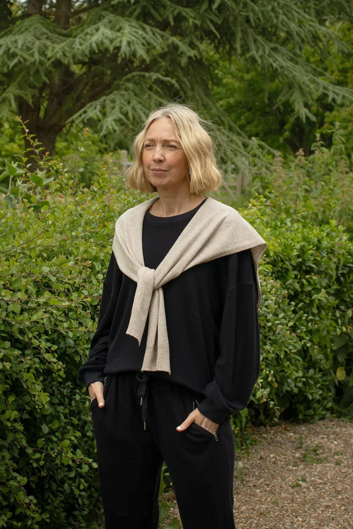 Woman wearing a beige scarf and navy blue jumper standing in a garden