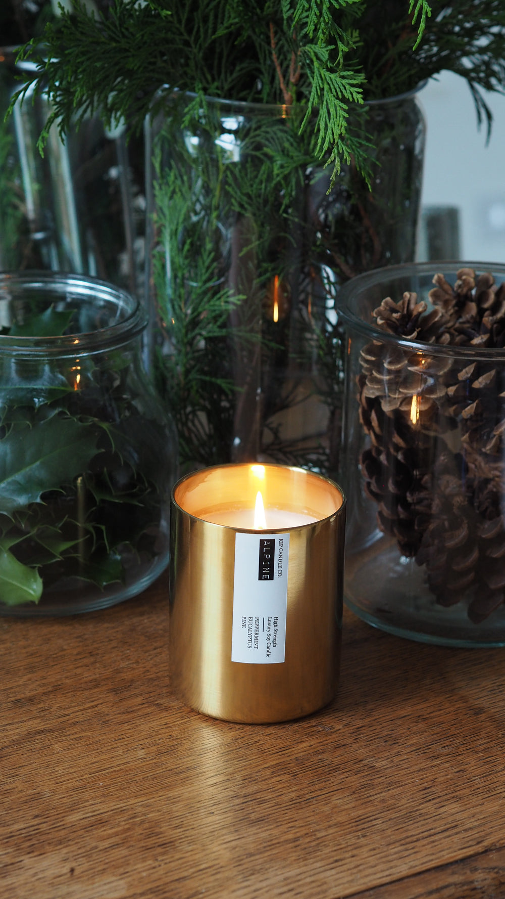 Gold candle holder with a label on a wooden surface next to greenery