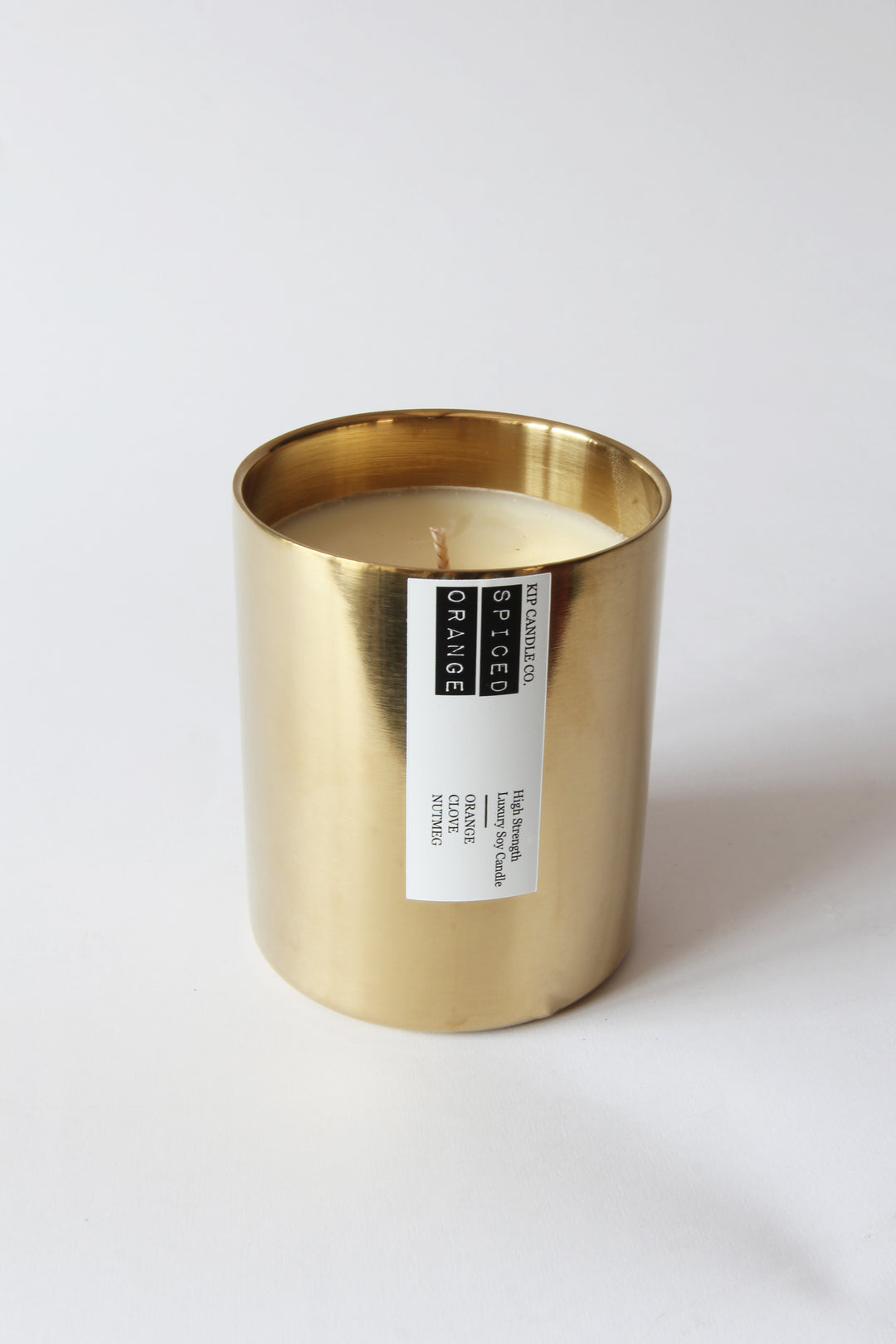 Gold candle holder with a white candle inside on a light gray background