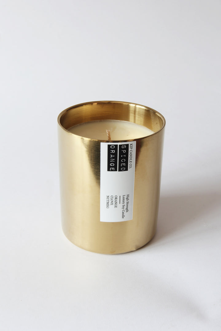 Gold candle holder with a white candle inside on a light gray background