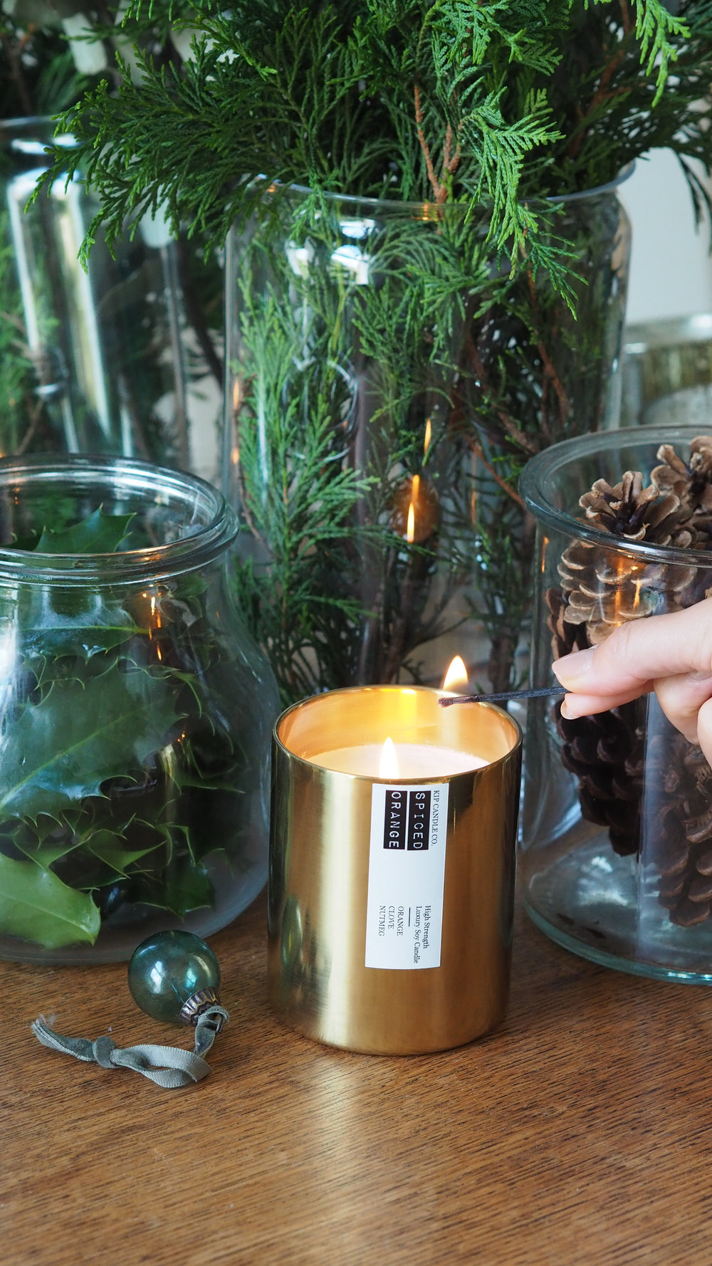 Candle being lit with a label on a wooden surface surrounded by greenery