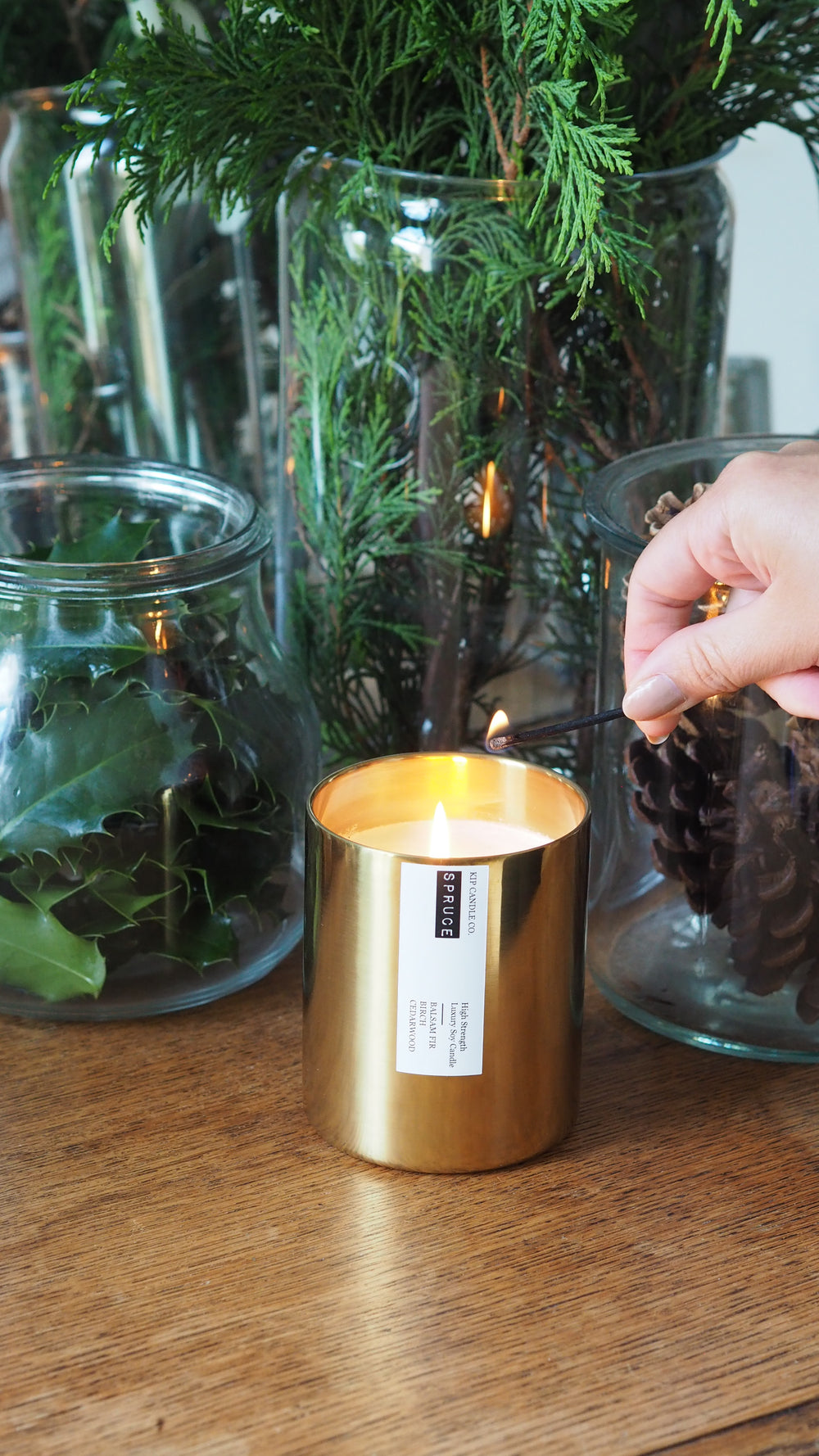 Gold candle holder with a label on a wooden surface next to greenery