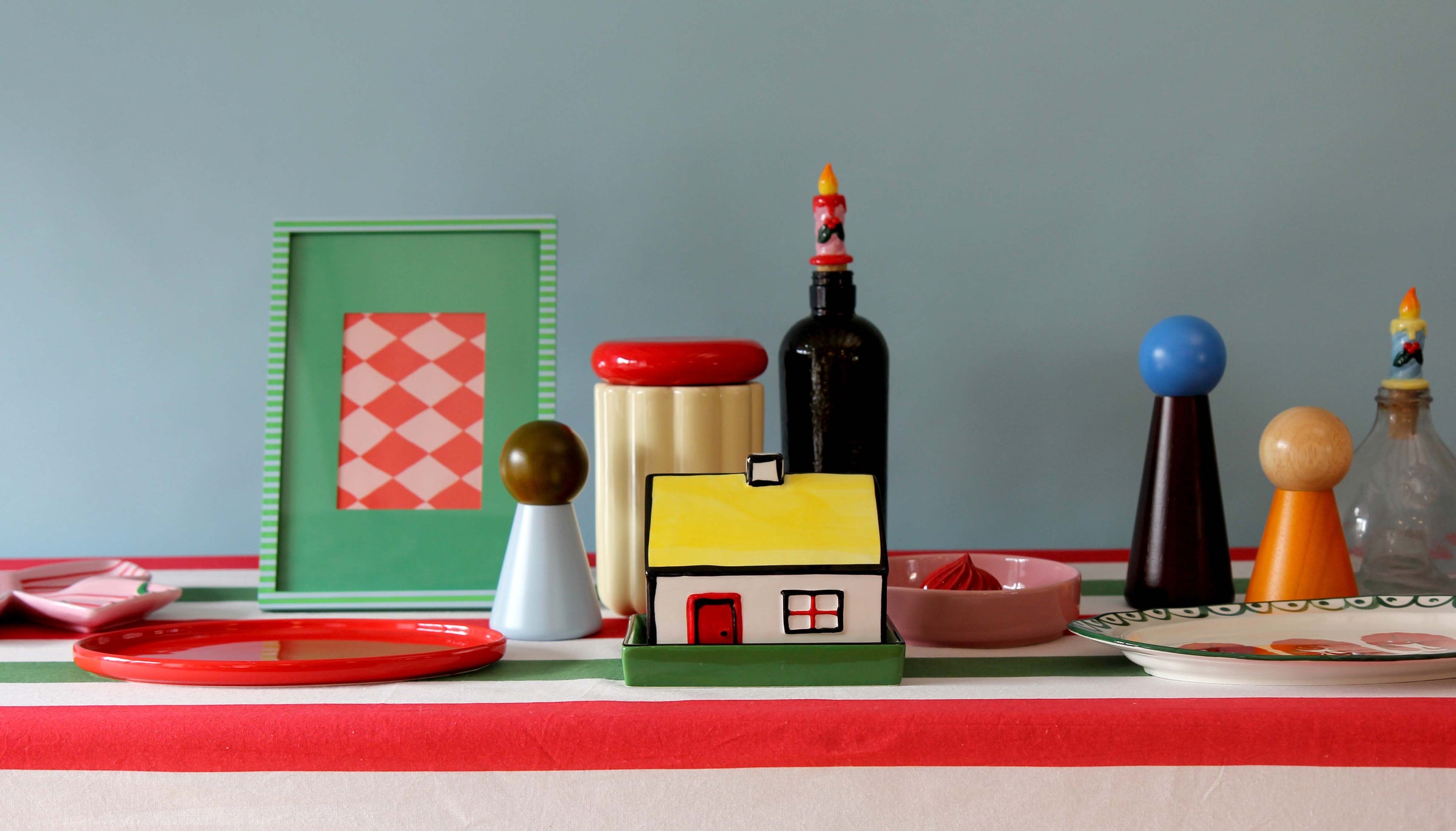 Colorful table setting with decorative items on a red tablecloth against a gray wall.
