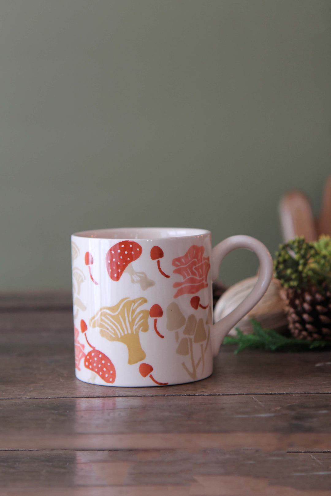 White mug with colorful floral pattern on a wooden surface with a green background