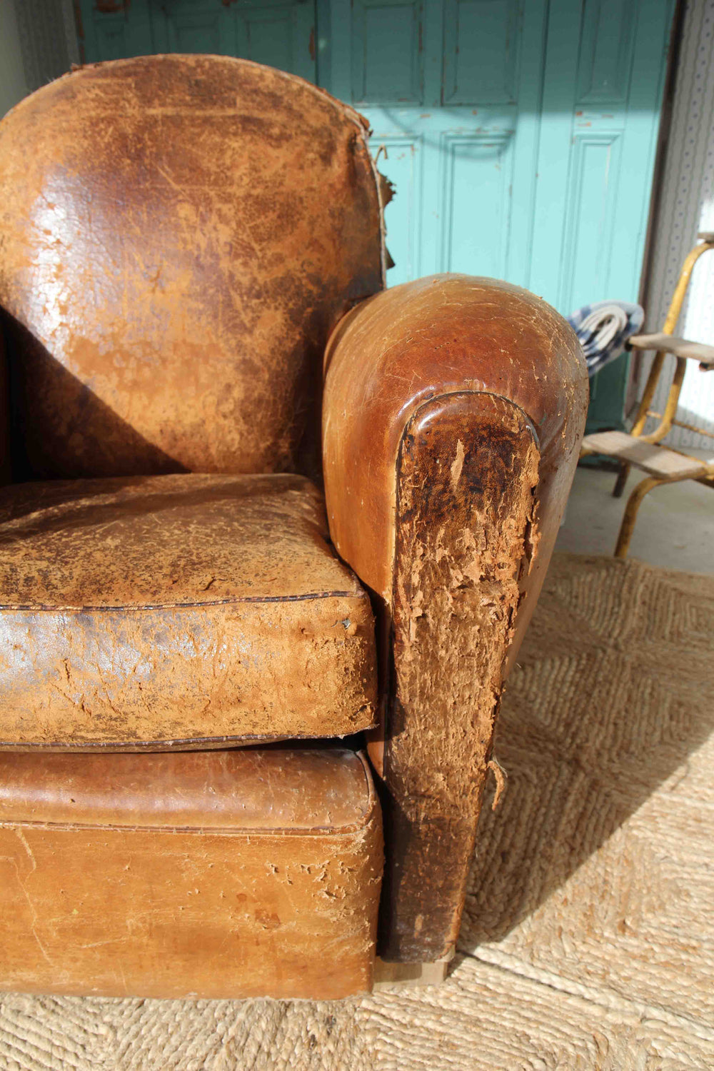 Worn brown leather armchair on a textured floor with a teal wall in the background.