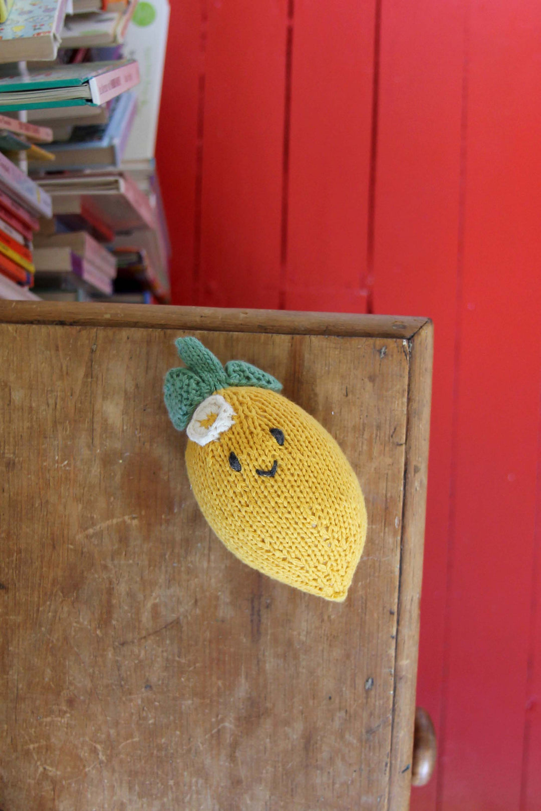 Knitted lemon-shaped toy on a wooden surface with a red background