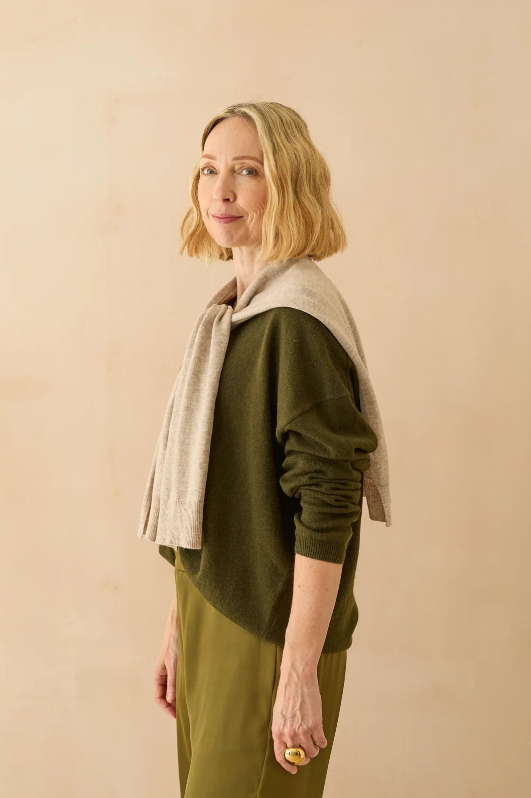 Woman wearing a green sweater and beige scarf against a beige background