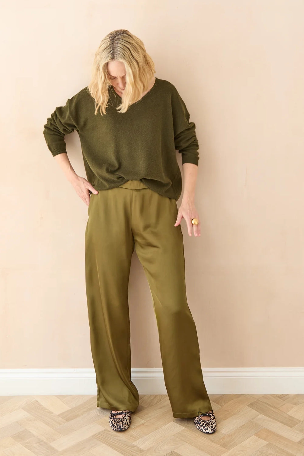 Woman wearing an olive green outfit standing against a beige wall.
