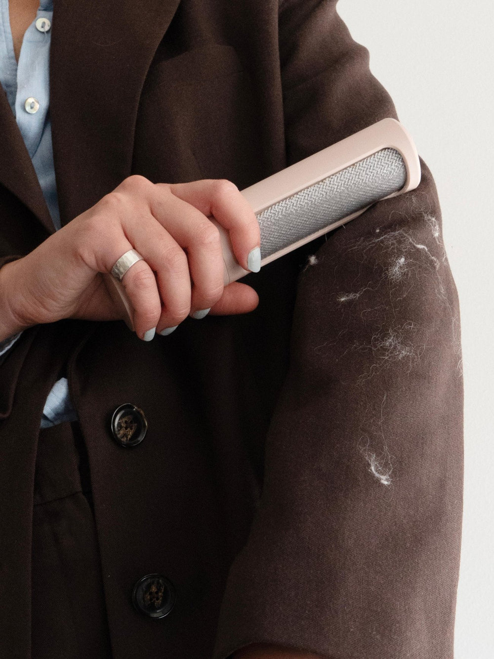Person using a lint remover on a brown coat against a white background