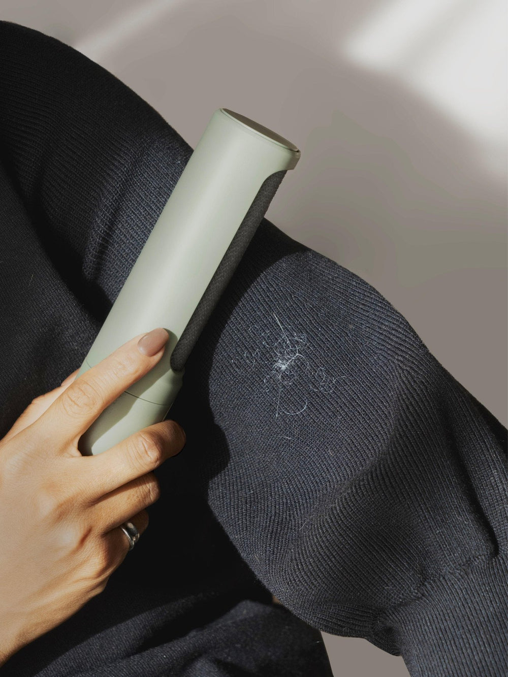 Person using a green and gray lint remover on a dark fabric.