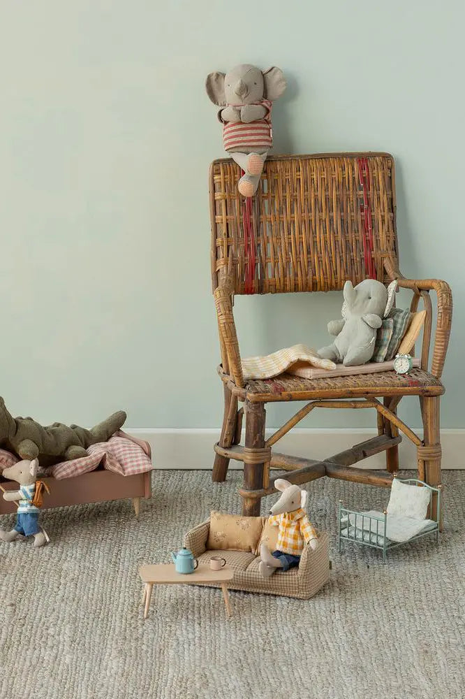 Children's room with wicker chair, sofa, and toys against a light green wall.