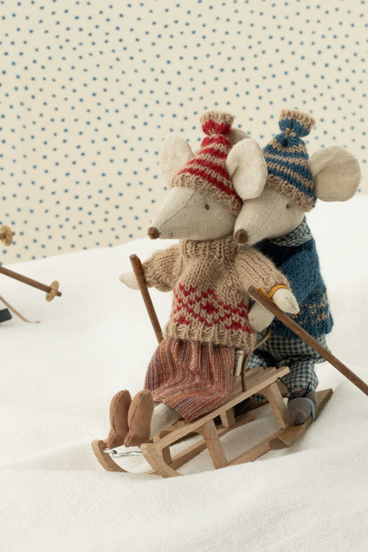 Two toy mice in winter clothing with skis and a sled on a polka dot background