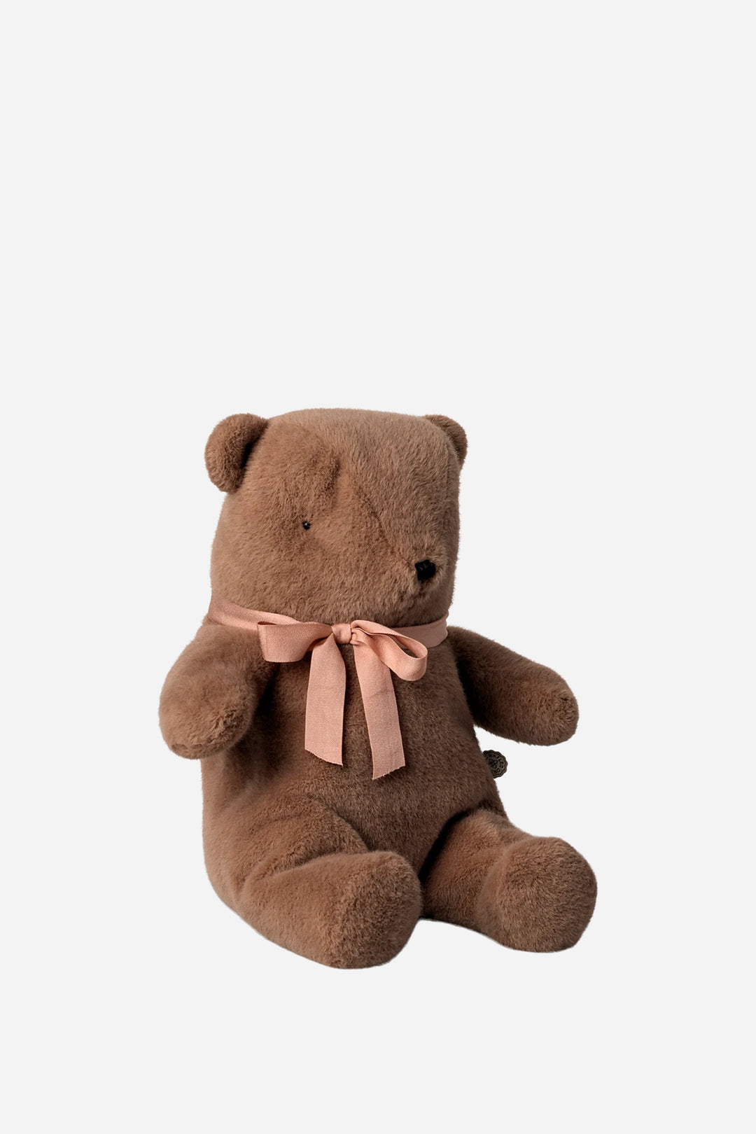 A brown plush teddy bear sitting upright, wearing a dusty pink satin bow around its neck, set against a solid light gray background.