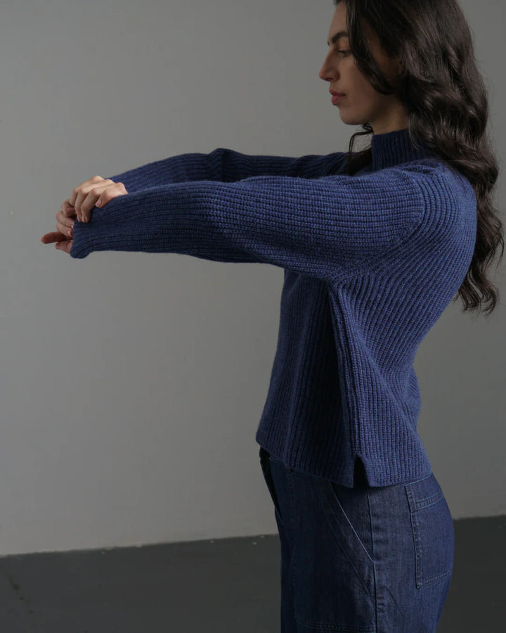 Woman wearing a blue ribbed sweater against a plain background