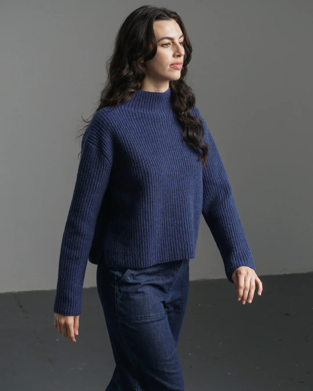 Woman wearing a blue sweater and pants against a gray background