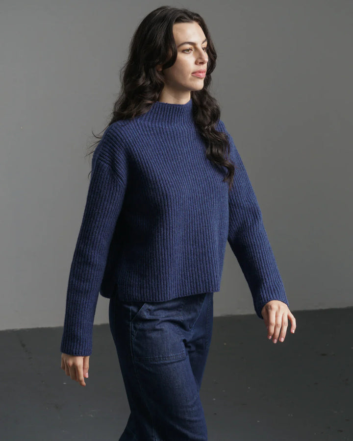 Woman wearing a blue sweater and pants against a gray background