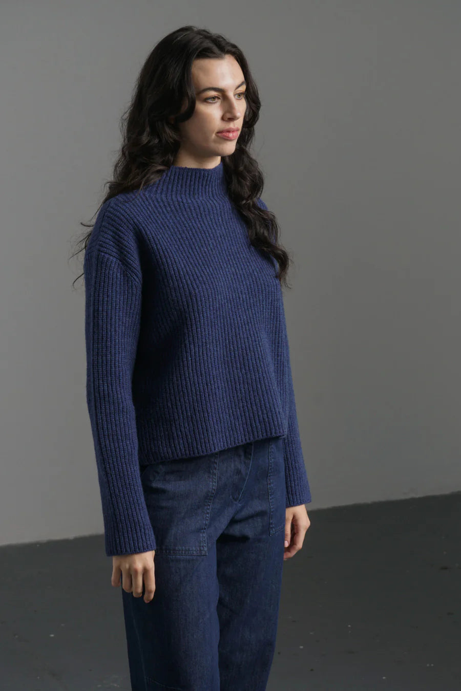 Woman wearing a blue sweater and pants against a gray background
