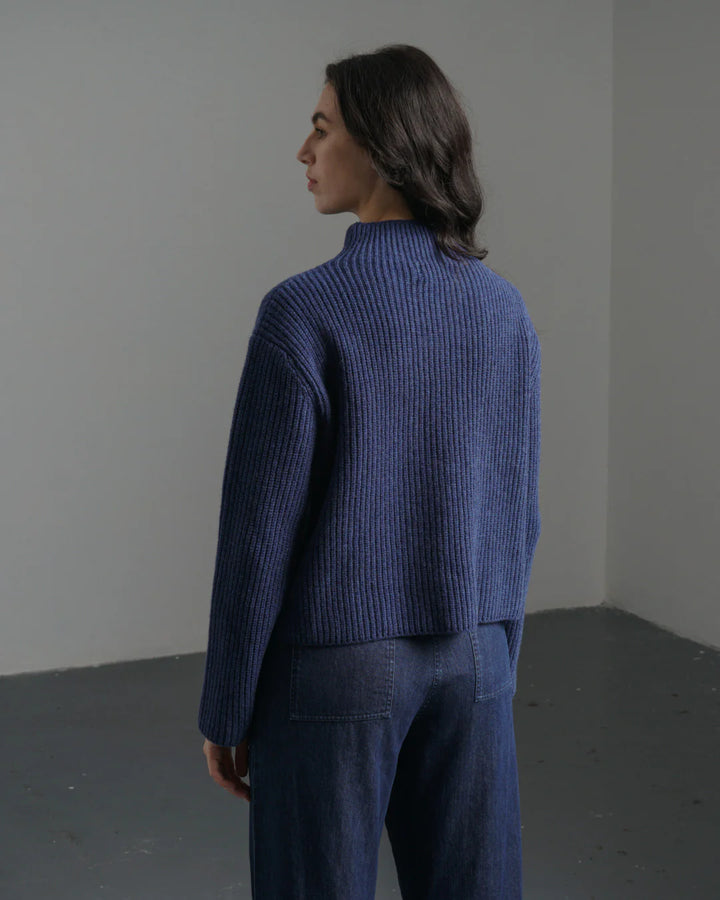 Person wearing a blue ribbed sweater and pants in a minimalistic setting