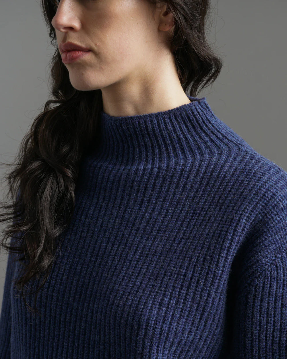 Person wearing a blue ribbed sweater against a neutral background