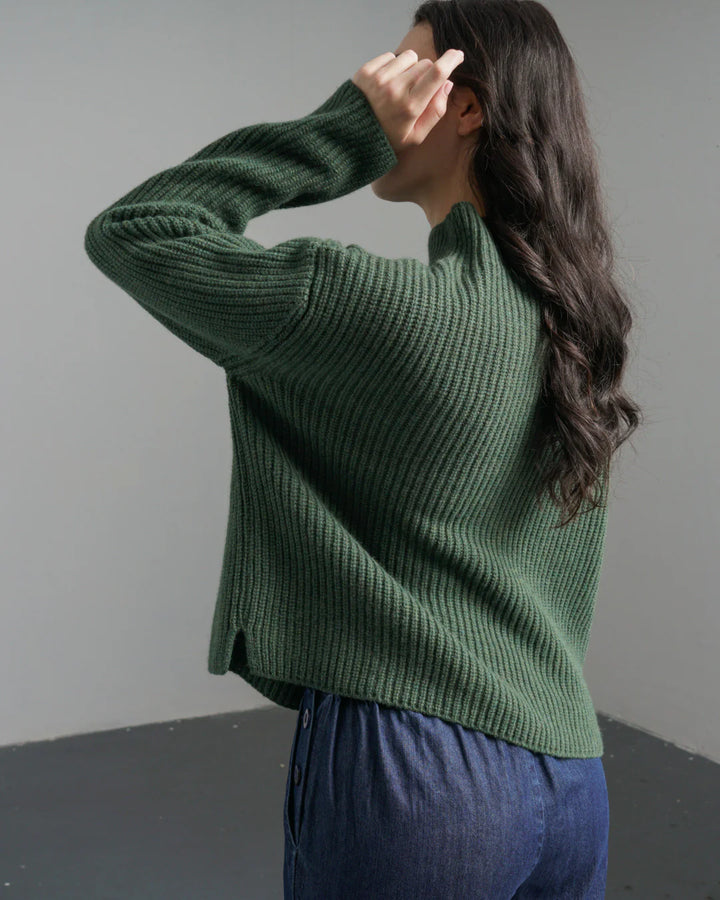 Person wearing a green sweater and blue pants against a plain background