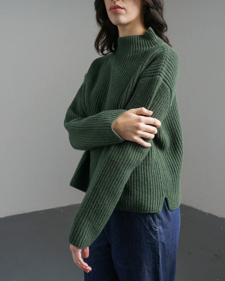 Person wearing a green sweater against a plain background